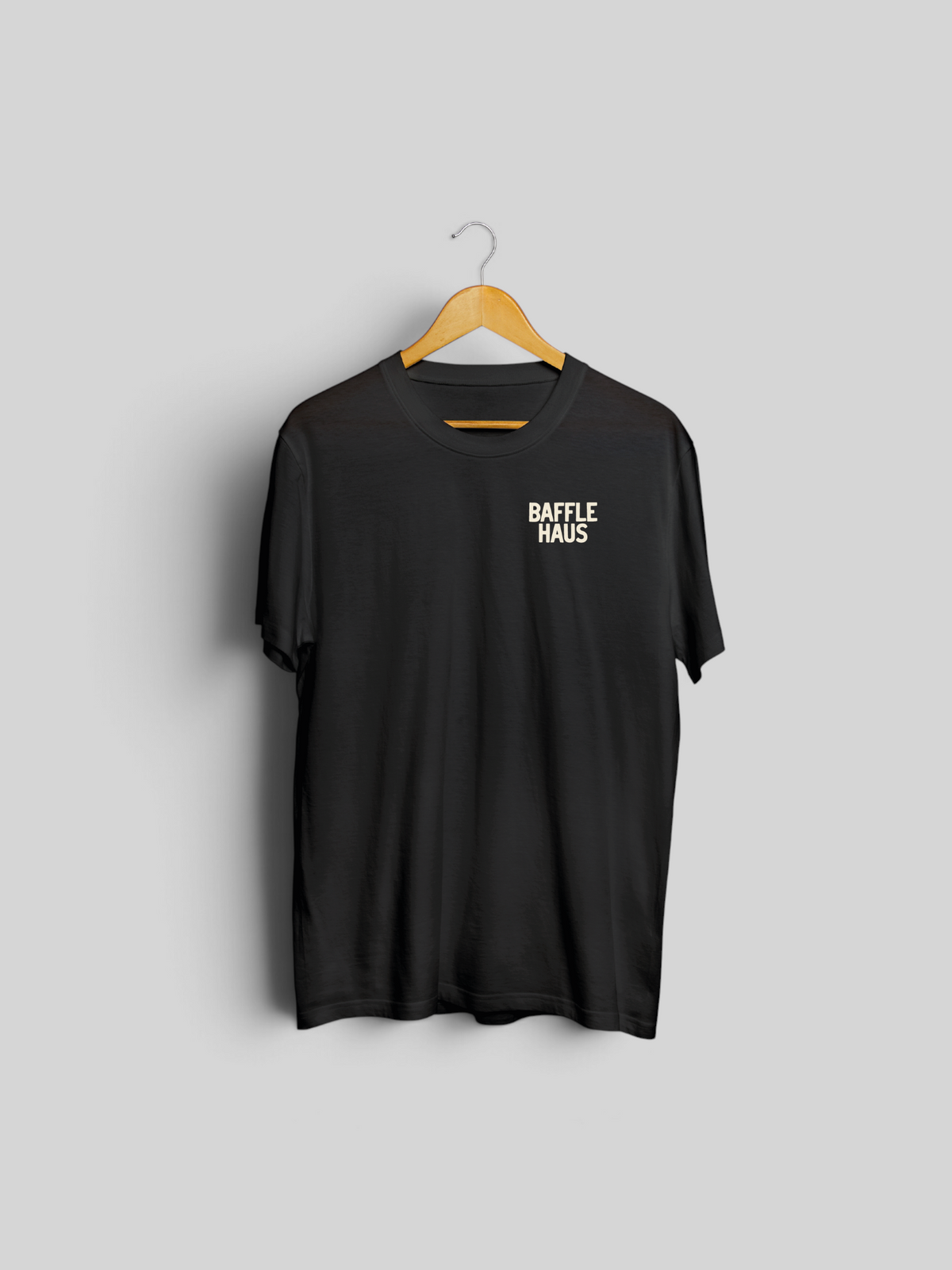 Baffle Haus black crew neck t-shirt with small white logo print on the chest hanging on a wooden hanger