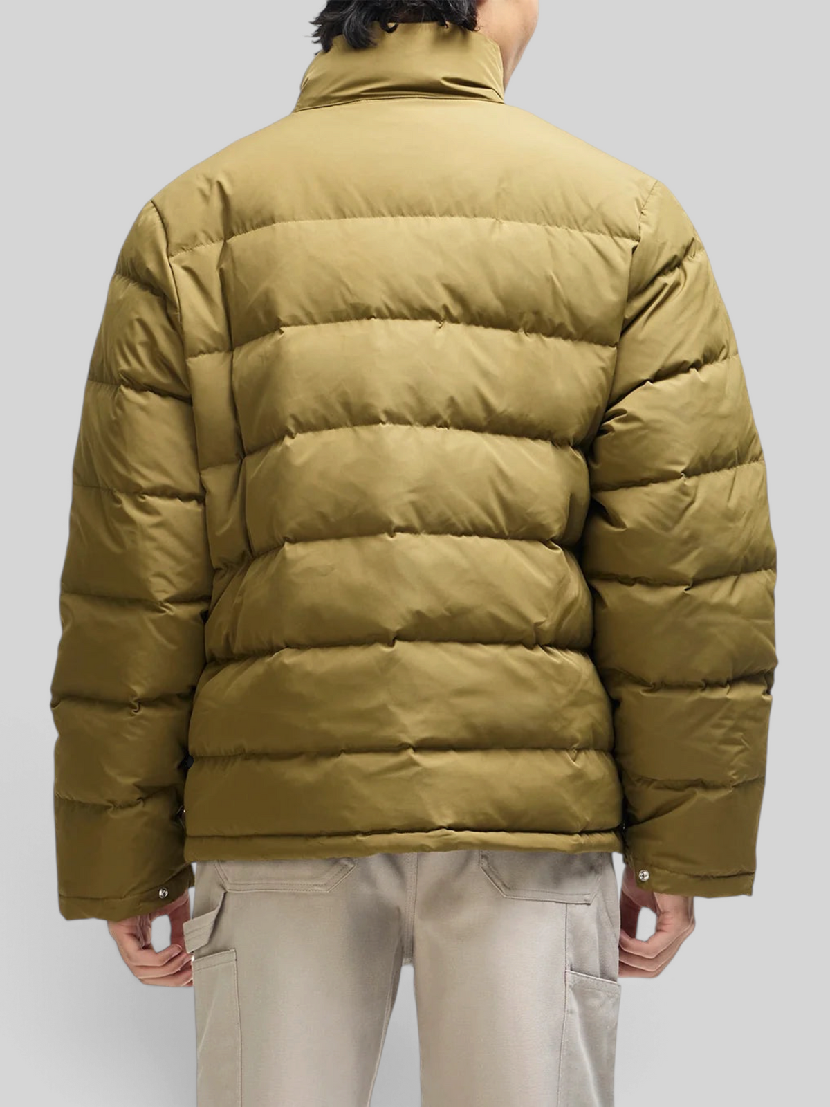 Back view of a person wearing a Baffle Haus olive green down jacket with a quilted design and high collar.