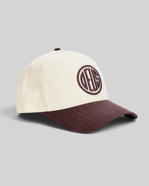 Baffle Haus 5-panel cap in cream cotton twill with a burgundy brim and circular embroidered logo detail.