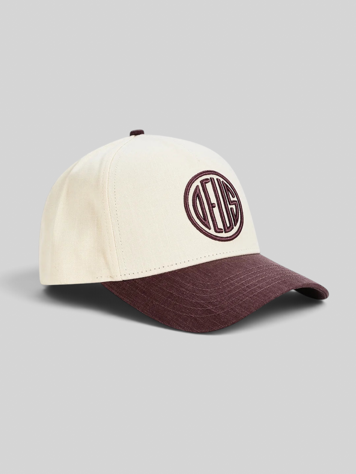 Baffle Haus 5-panel cap in cream cotton twill with a burgundy brim and circular embroidered logo detail.