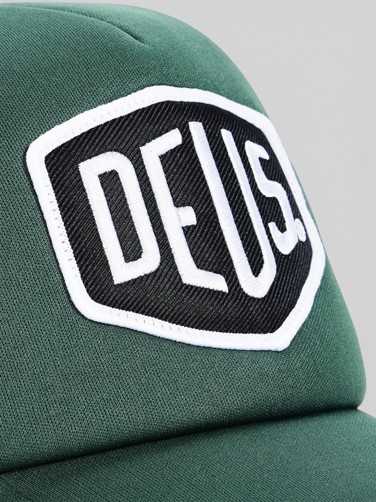 Baffle Haus Baylands trucker cap in racing green with a white and black embroidered Deus logo patch on the front