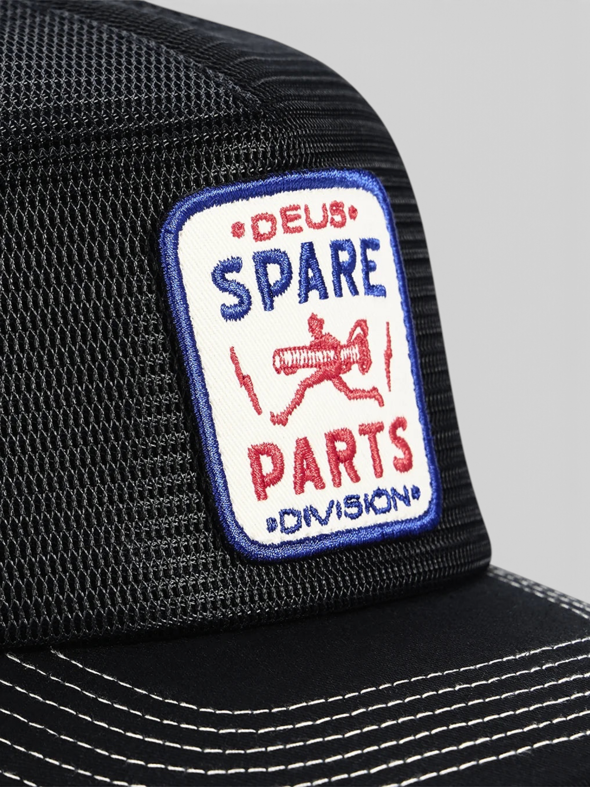 Baffle Haus Mudflap Trucker cap in black featuring a detailed embroidered Deus Spare Parts badge on polyester mesh