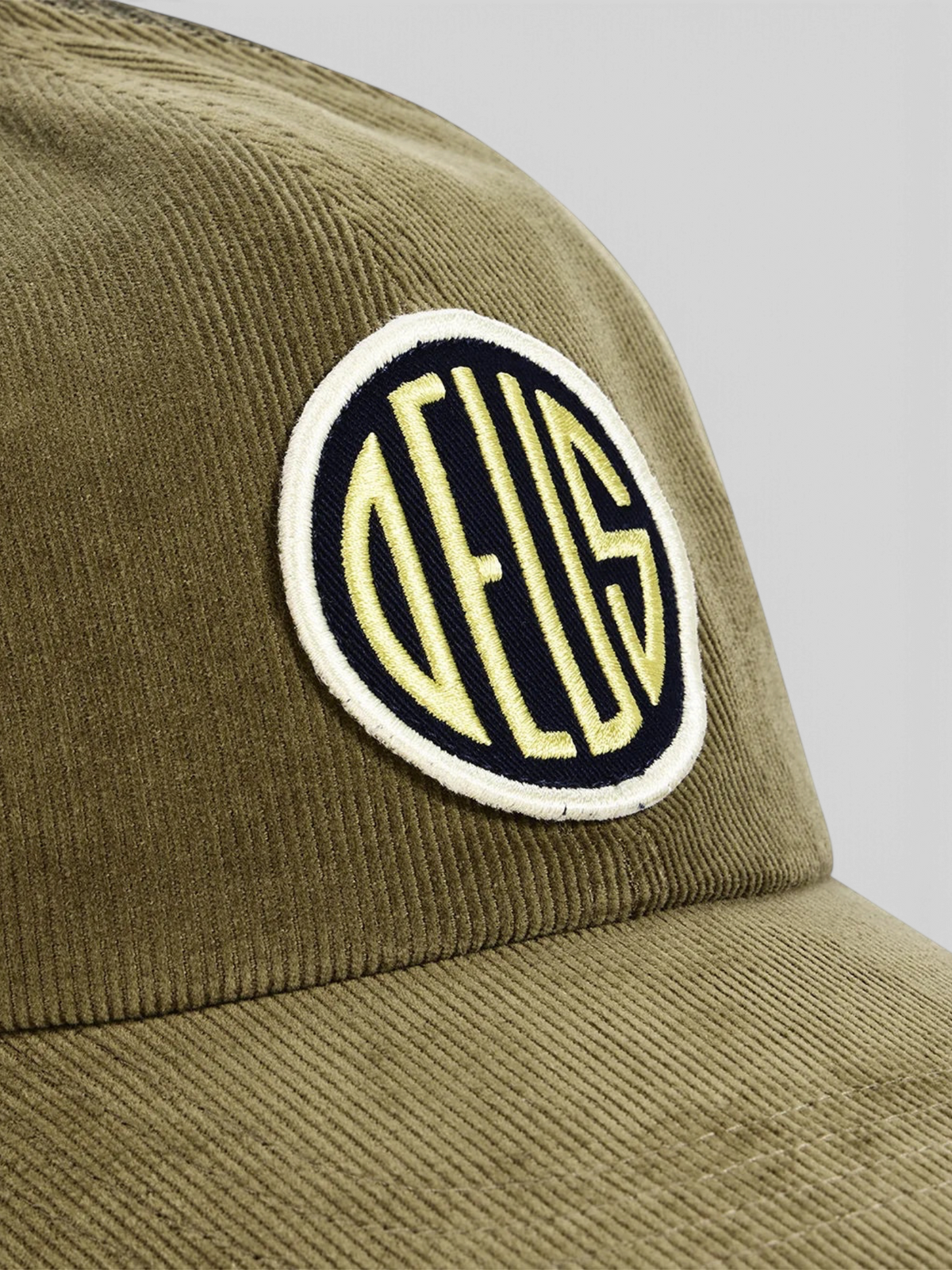 Baffle Haus olive green cotton corduroy trucker hat with a circular embroidered logo patch on the front