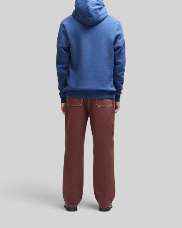 Baffle Haus Mudflap Hoodie in mechanic blue organic cotton fleece, back view on a model wearing brown trousers.