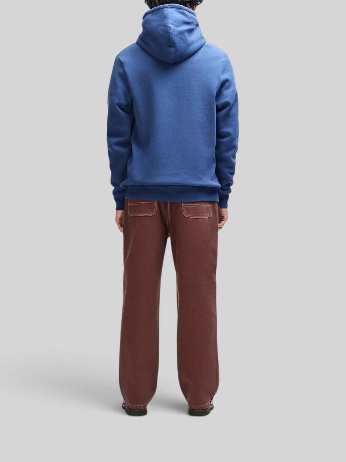 Baffle Haus Mudflap Hoodie in mechanic blue organic cotton fleece, back view on a model wearing brown trousers.