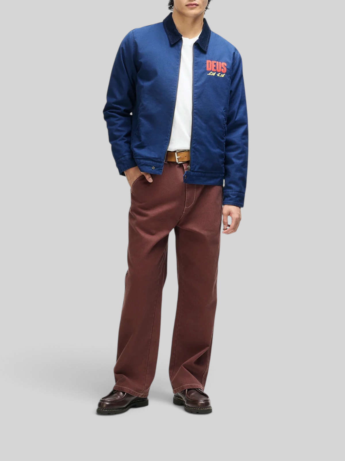 A model wearing a Baffle Haus navy cotton whipcord cutaway jacket with red chest embroidery and a corduroy collar.