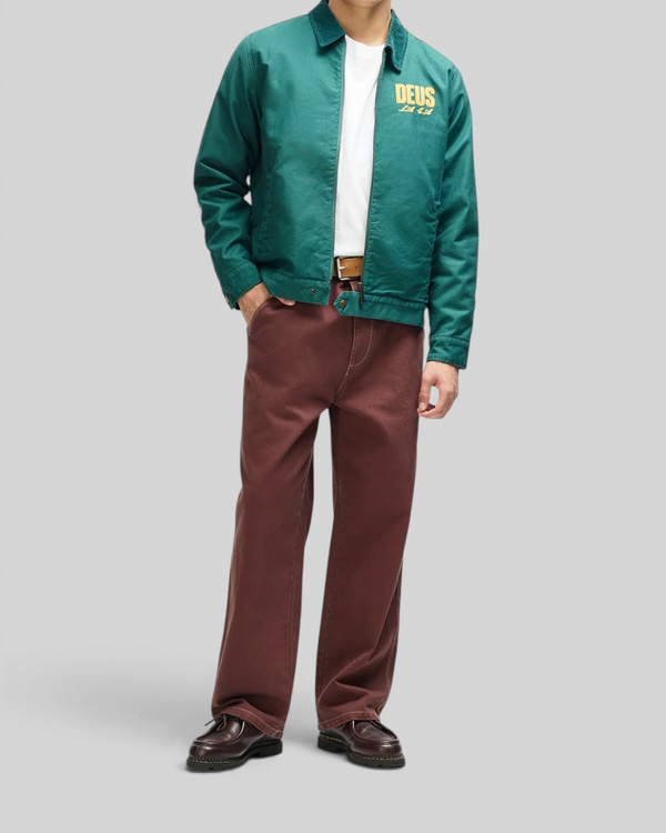 Model wearing a Baffle Haus racing green cotton whipcord cutaway jacket with embroidered chest art and zip closure.