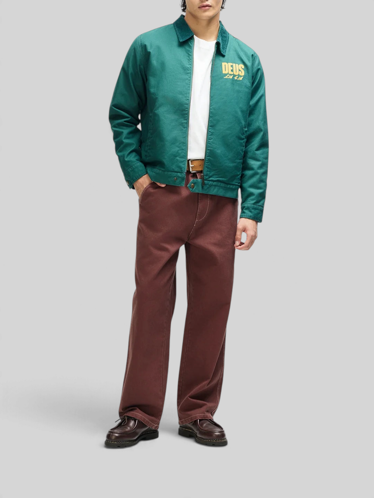Model wearing a Baffle Haus racing green cotton whipcord cutaway jacket with embroidered chest art and zip closure.
