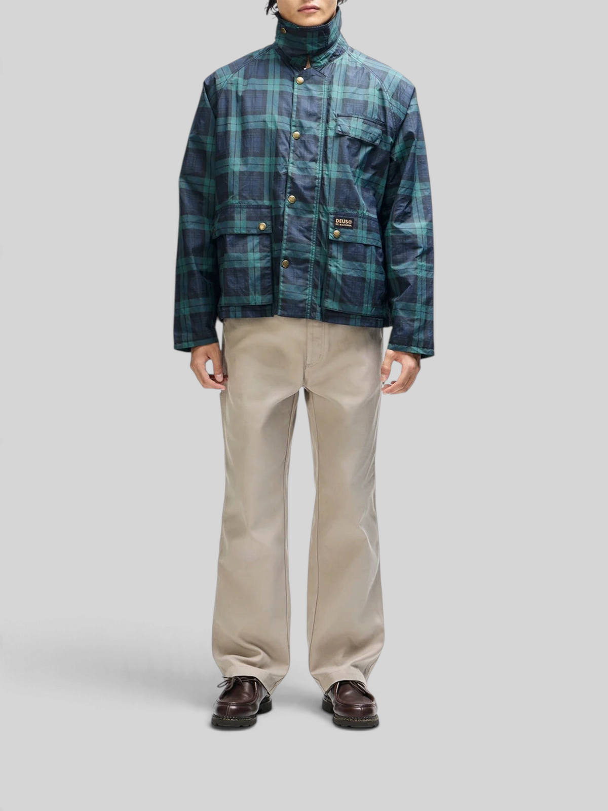 Baffle Haus Marsden hunting jacket in green check with corduroy collar, worn with beige trousers.