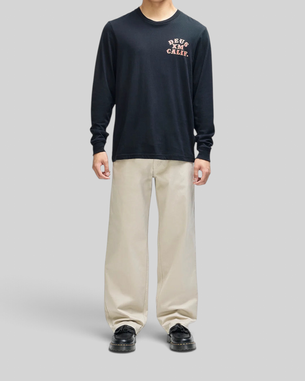 Baffle Haus black long sleeve tee with chest graphic, box fit, worn by a model with beige trousers.