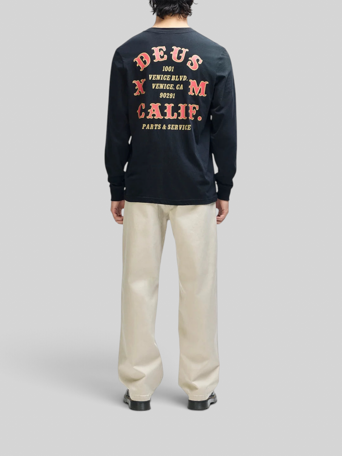 Baffle Haus black long sleeve tee with red and yellow graphic print on the back, worn by a man with light trousers.