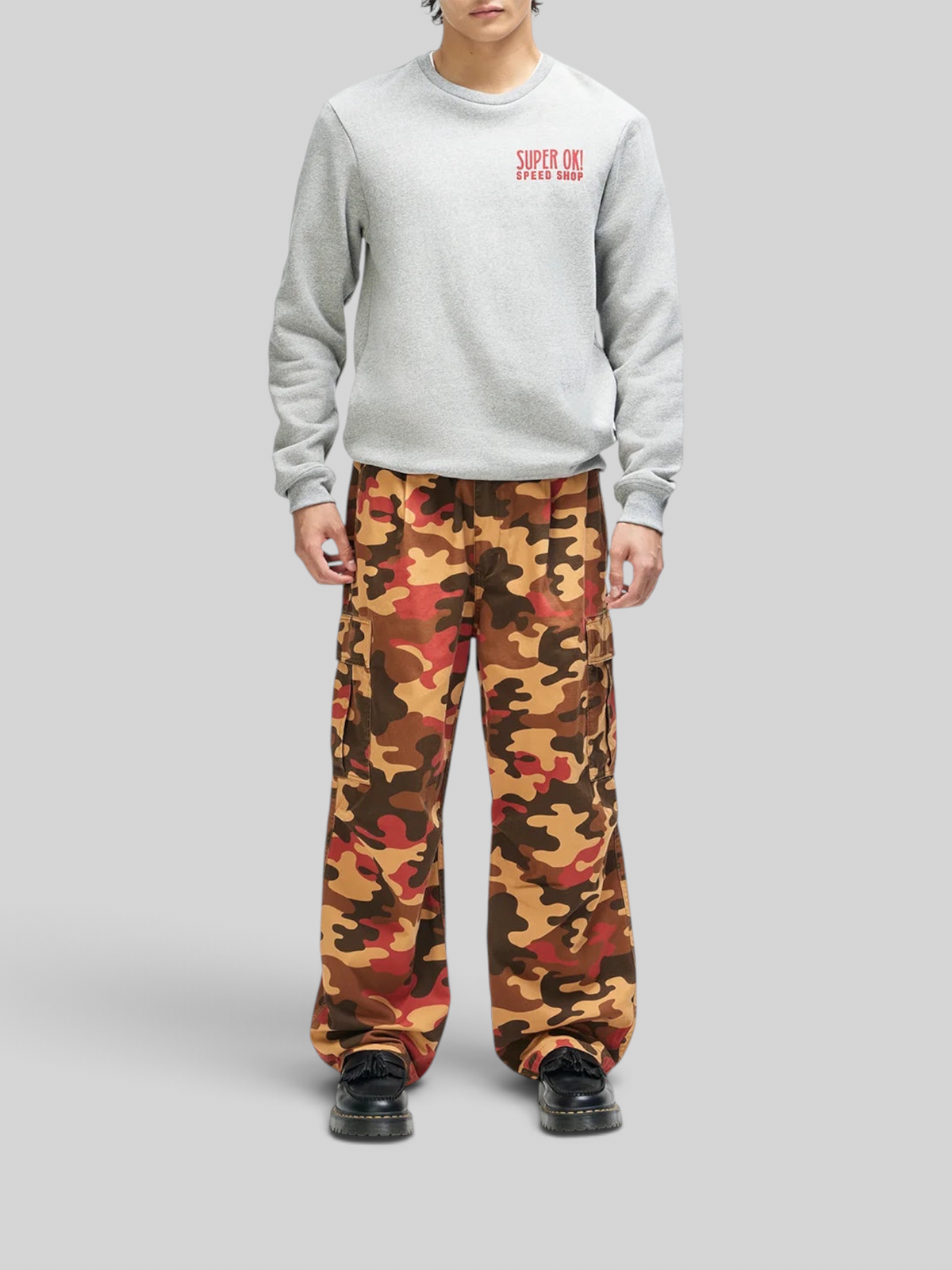 Baffle Haus model wearing a grey marle box fit sweatshirt with red chest graphic and multi-coloured camo cargo pants