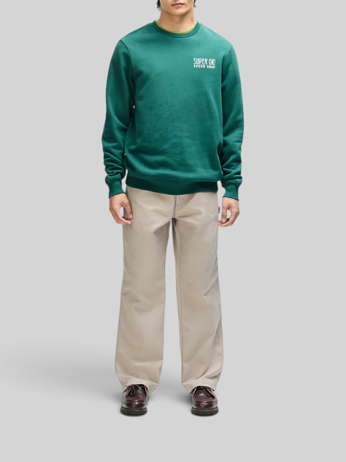 Baffle Haus Chessboxin Crew sweatshirt in racing green with chest graphic, worn with beige trousers.