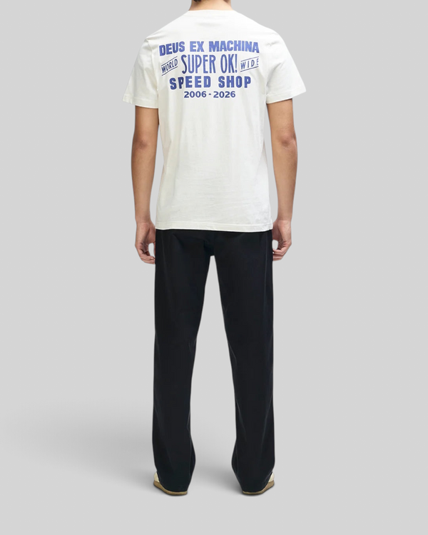 Baffle Haus Mudflap Tee in vintage white with blue graphic print on the back, worn by a man with black trousers.