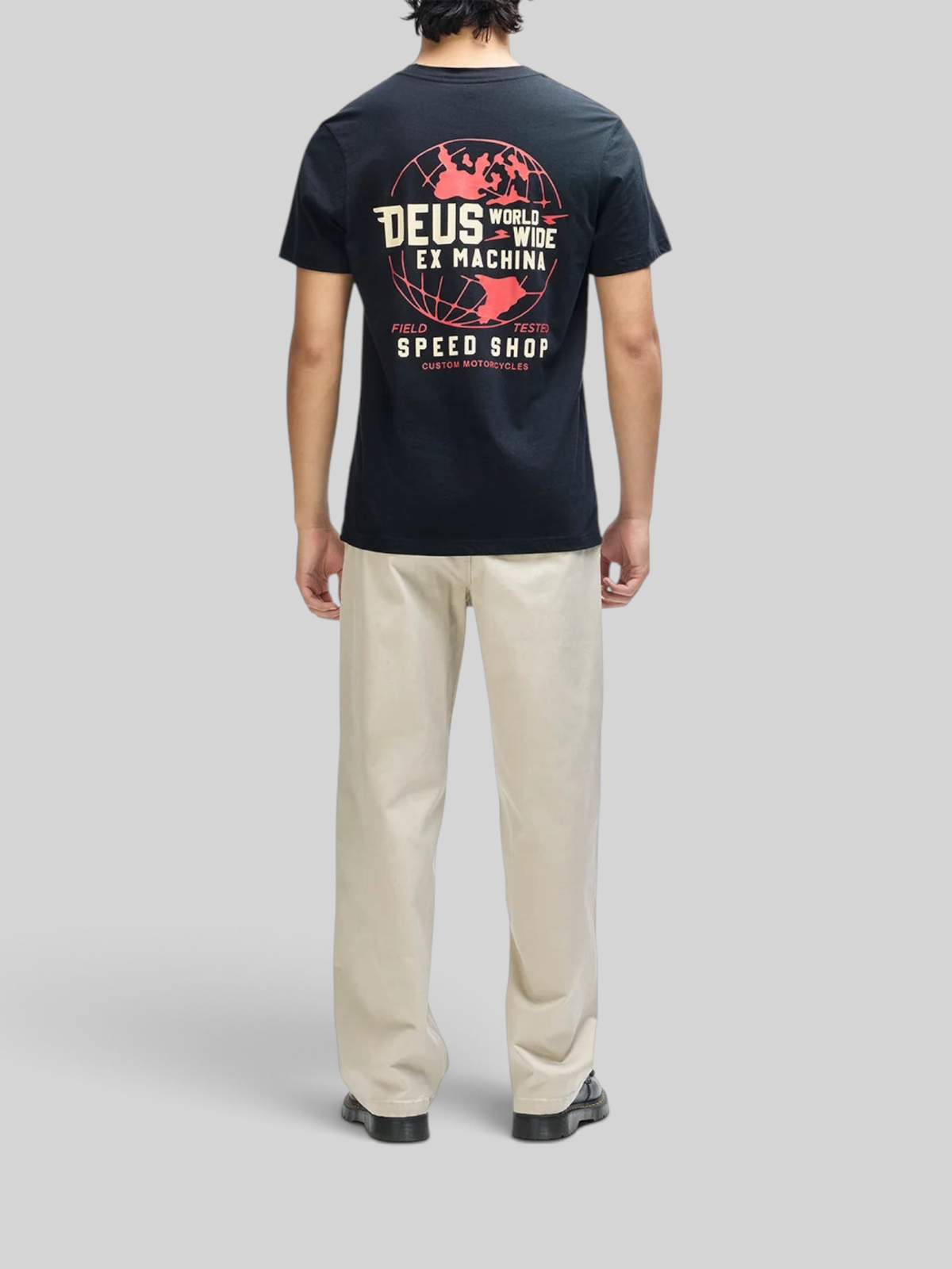 Baffle Haus Global Spark black box fit t-shirt with red and cream globe graphic on back, worn with beige trousers.