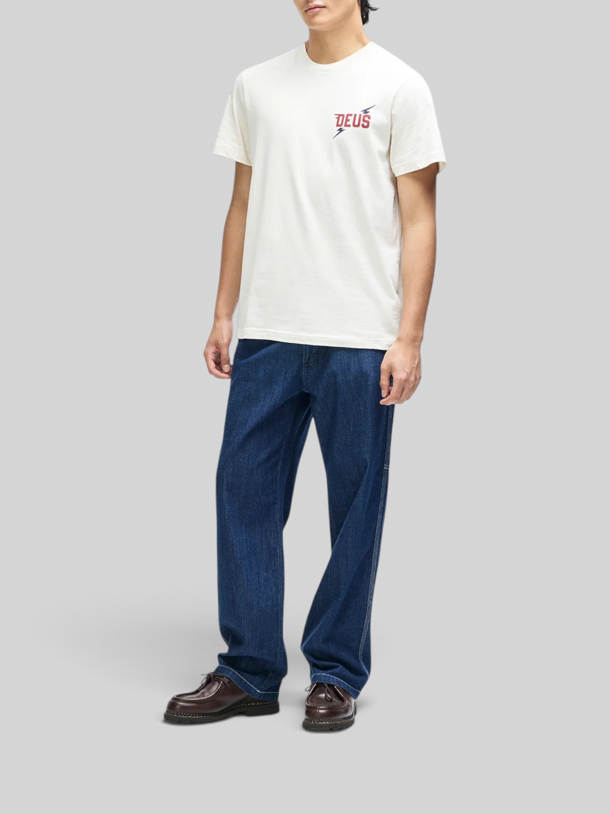 Baffle Haus Global Spark Tee in vintage white organic cotton with chest graphic, worn by a model with blue jeans.