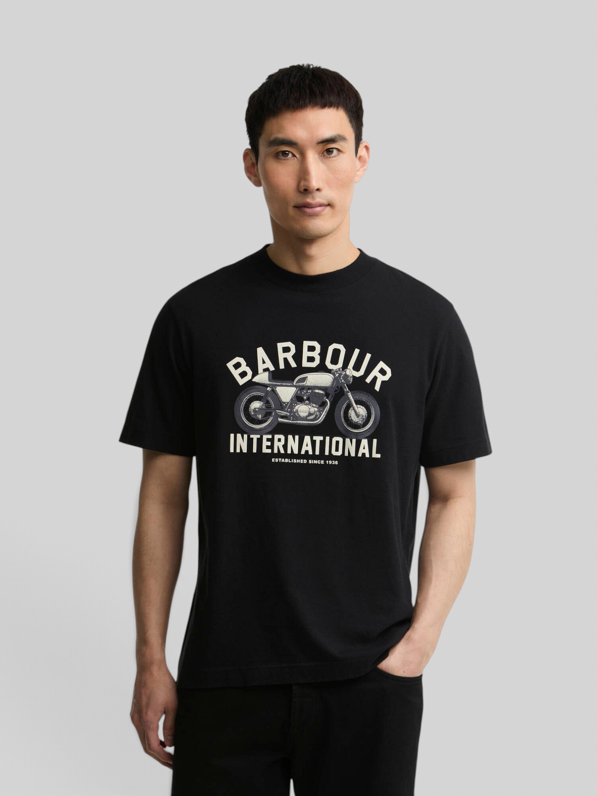 A man wearing a black Baffle Haus Eric graphic cotton t-shirt featuring a vintage motorcycle print on the chest.
