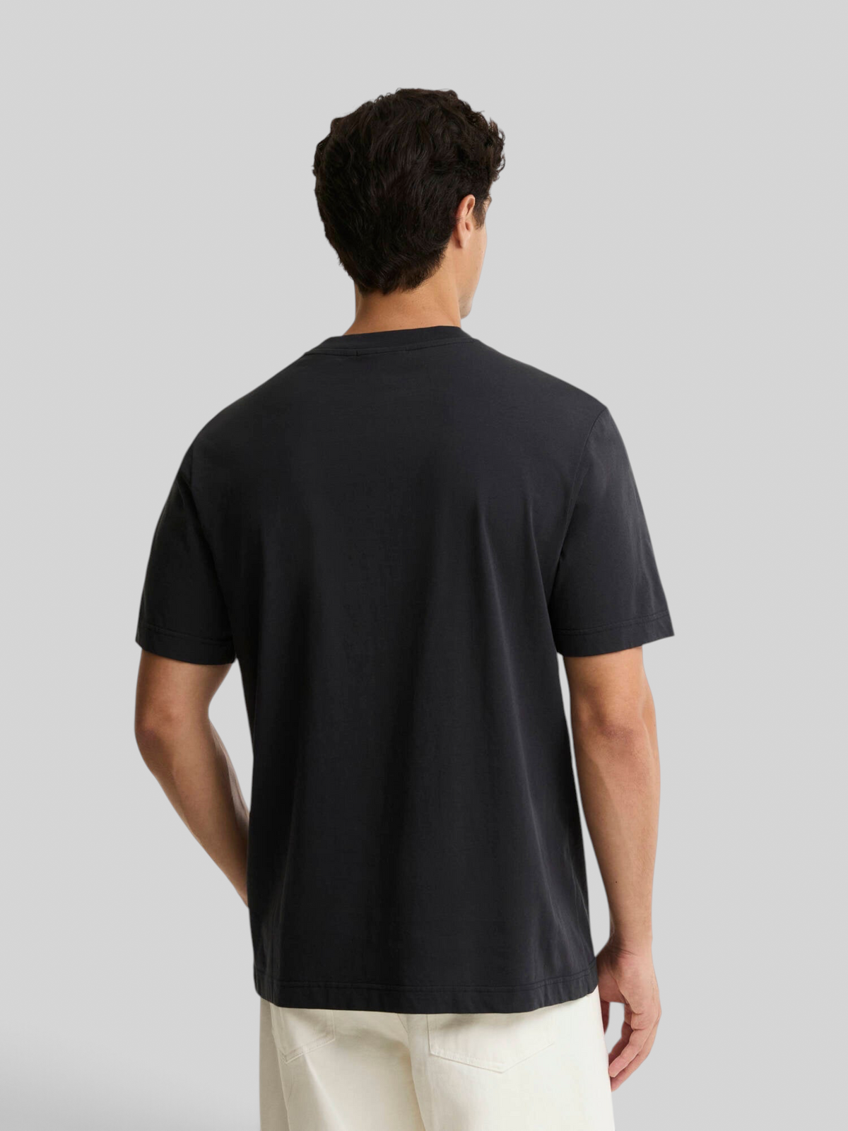 Back view of a man wearing a plain black Baffle Haus cotton crew neck t-shirt with short sleeves