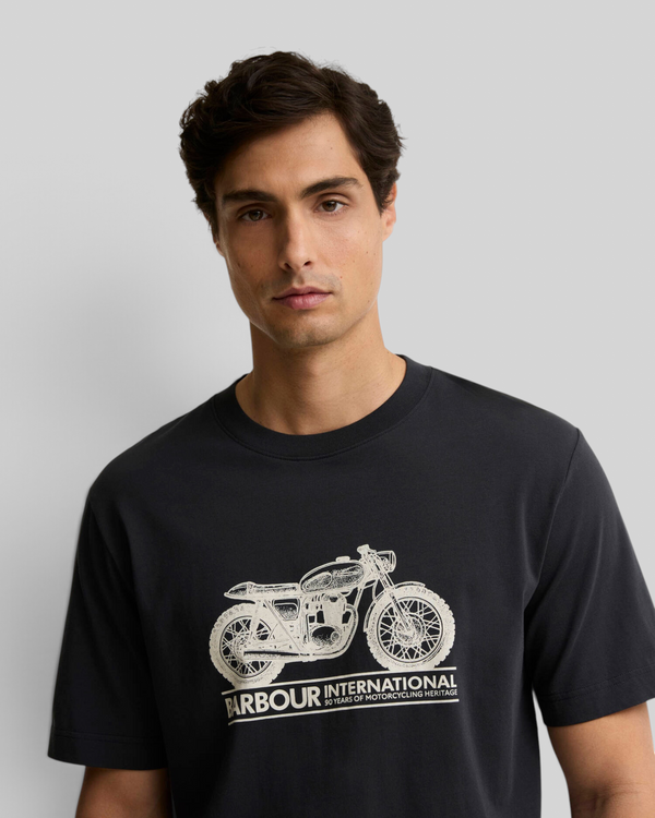 A man wearing a black Baffle Haus Barbour International cotton t-shirt featuring a white vintage motorbike graphic.