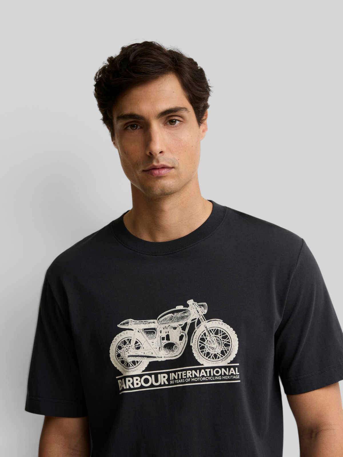 A man wearing a black Baffle Haus Barbour International cotton t-shirt featuring a white vintage motorbike graphic.