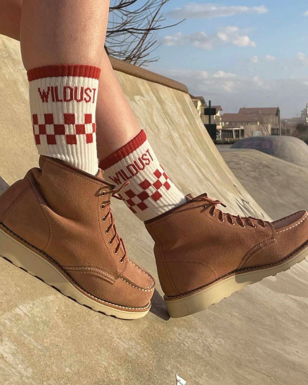 Baffle Haus brick red and cream checkered race socks worn with tan suede boots in a skatepark setting
