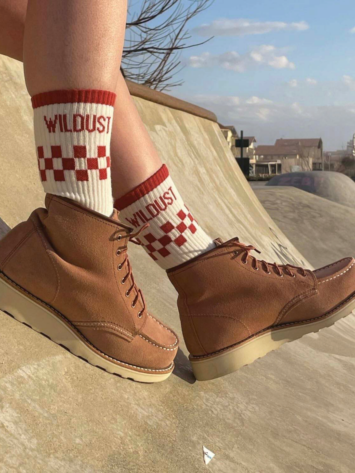 Baffle Haus brick red and cream checkered race socks worn with tan suede boots in a skatepark setting