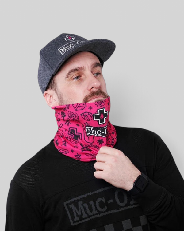 Baffle Haus pink neck tube with punk-inspired graphics worn by a man in a grey cap and black long-sleeve shirt