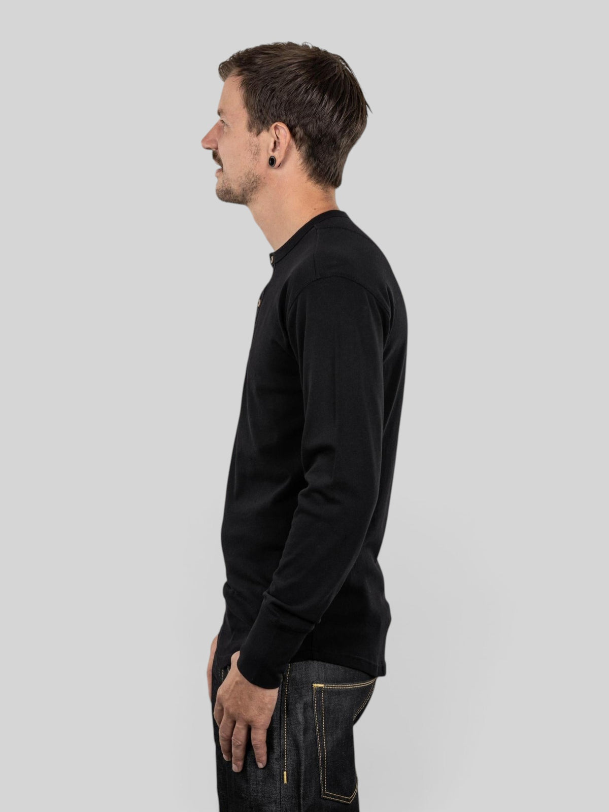 Baffle Haus 1927 Henley long sleeve shirt in deep black cotton with coconut buttons, worn by a man, side profile view.