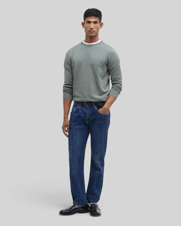 Baffle Haus model wearing an agave green Pima cotton crew neck sweater with embroidered logo over blue jeans