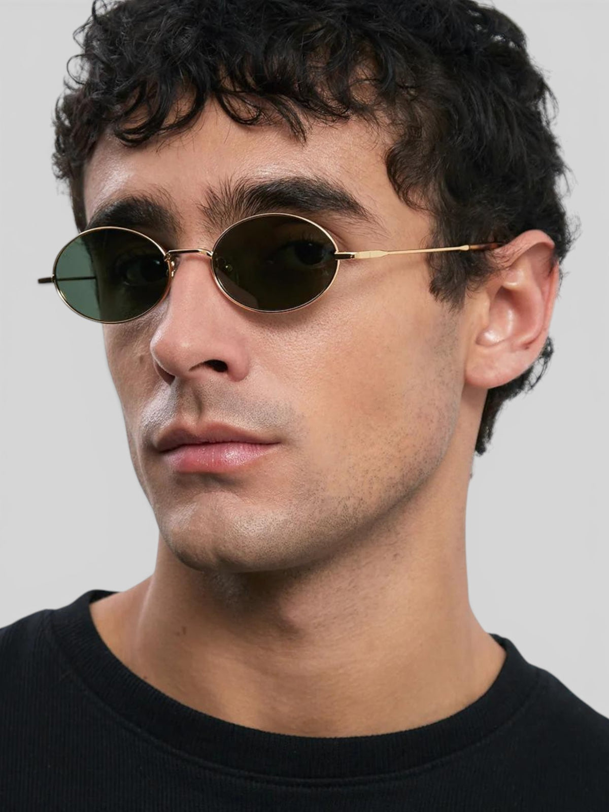 Baffle Haus Amara sunglasses with slim gold stainless steel oval frames and dark polarized lenses on a male model