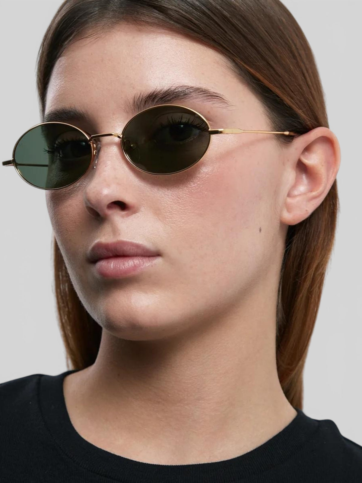 Baffle Haus Amara oval sunglasses with slim gold stainless steel frames and dark polarized lenses on a model
