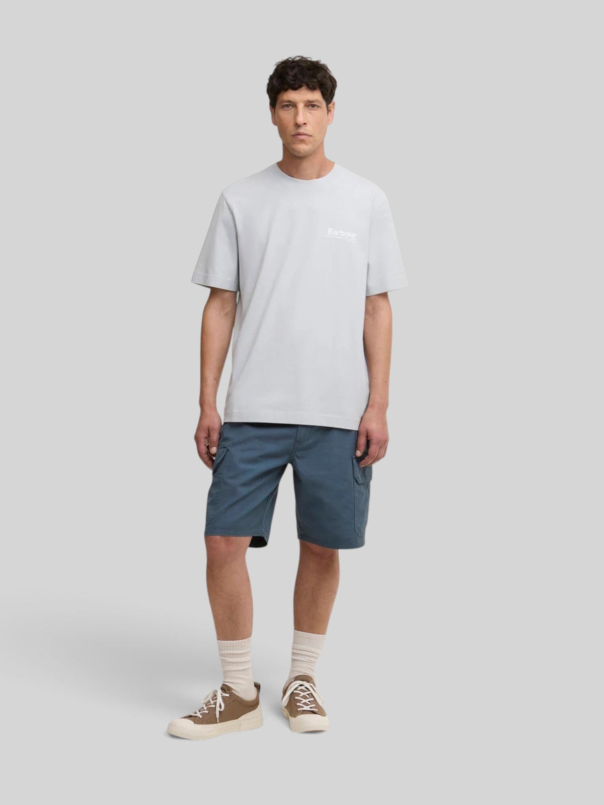 Baffle Haus model wearing a light blue Barbour Wildfell cotton graphic t-shirt with blue cargo shorts and sneakers.