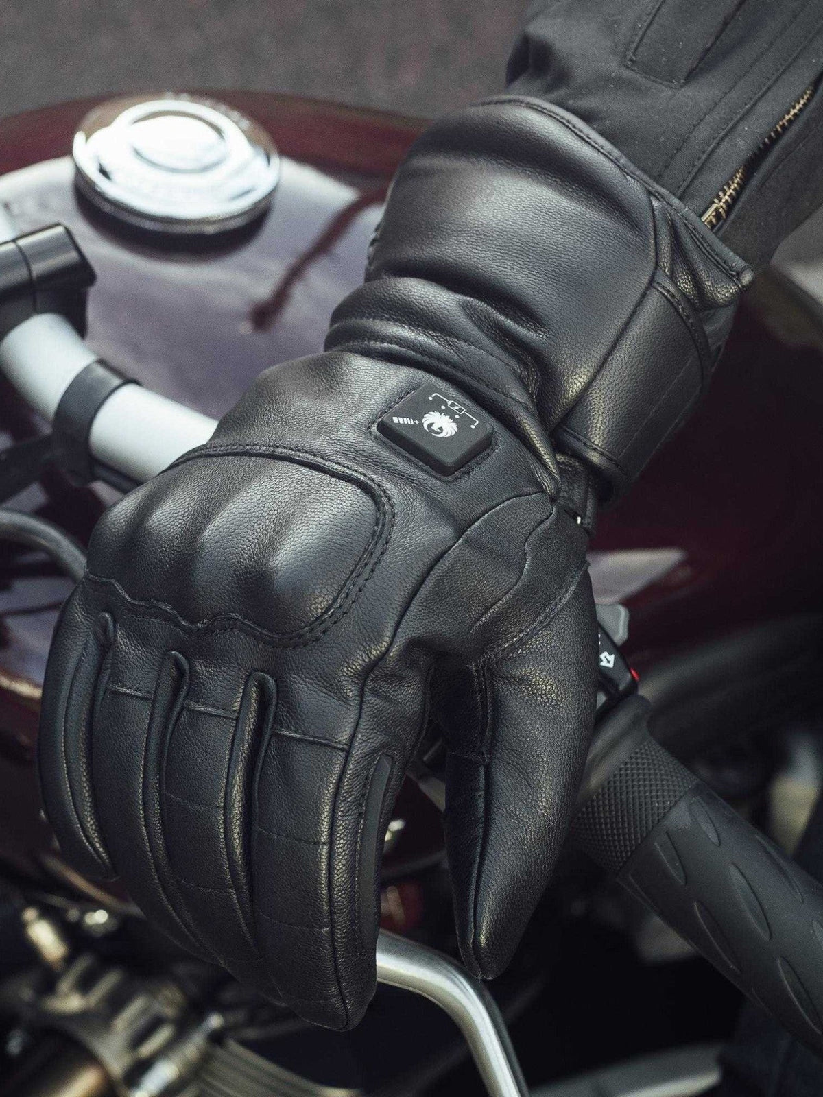 Baffle Haus Bednell black leather heated motorcycle glove with back of hand controller on a bike handlebar