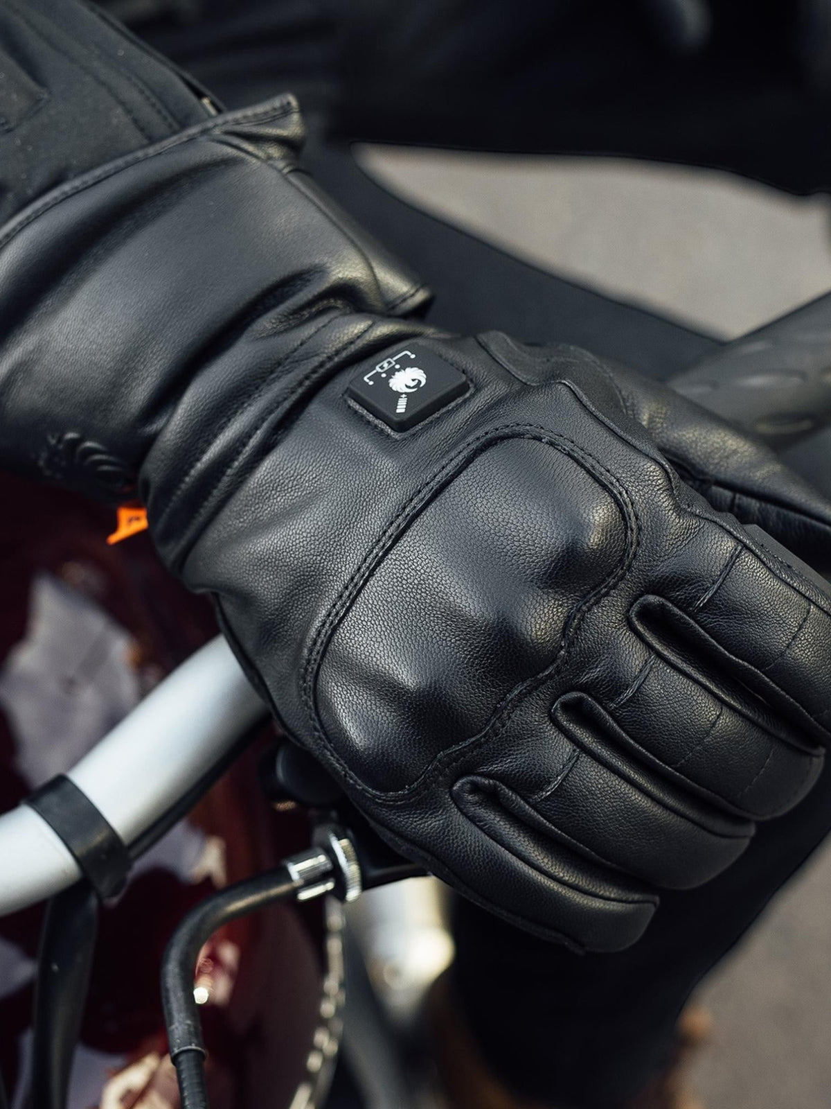 Baffle Haus Bednell black leather heated motorcycle glove with back of hand controller on a bike handlebar