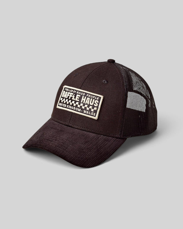 Baffle Haus black corduroy trucker cap with breathable mesh back and branded rectangular patch on the front panel.