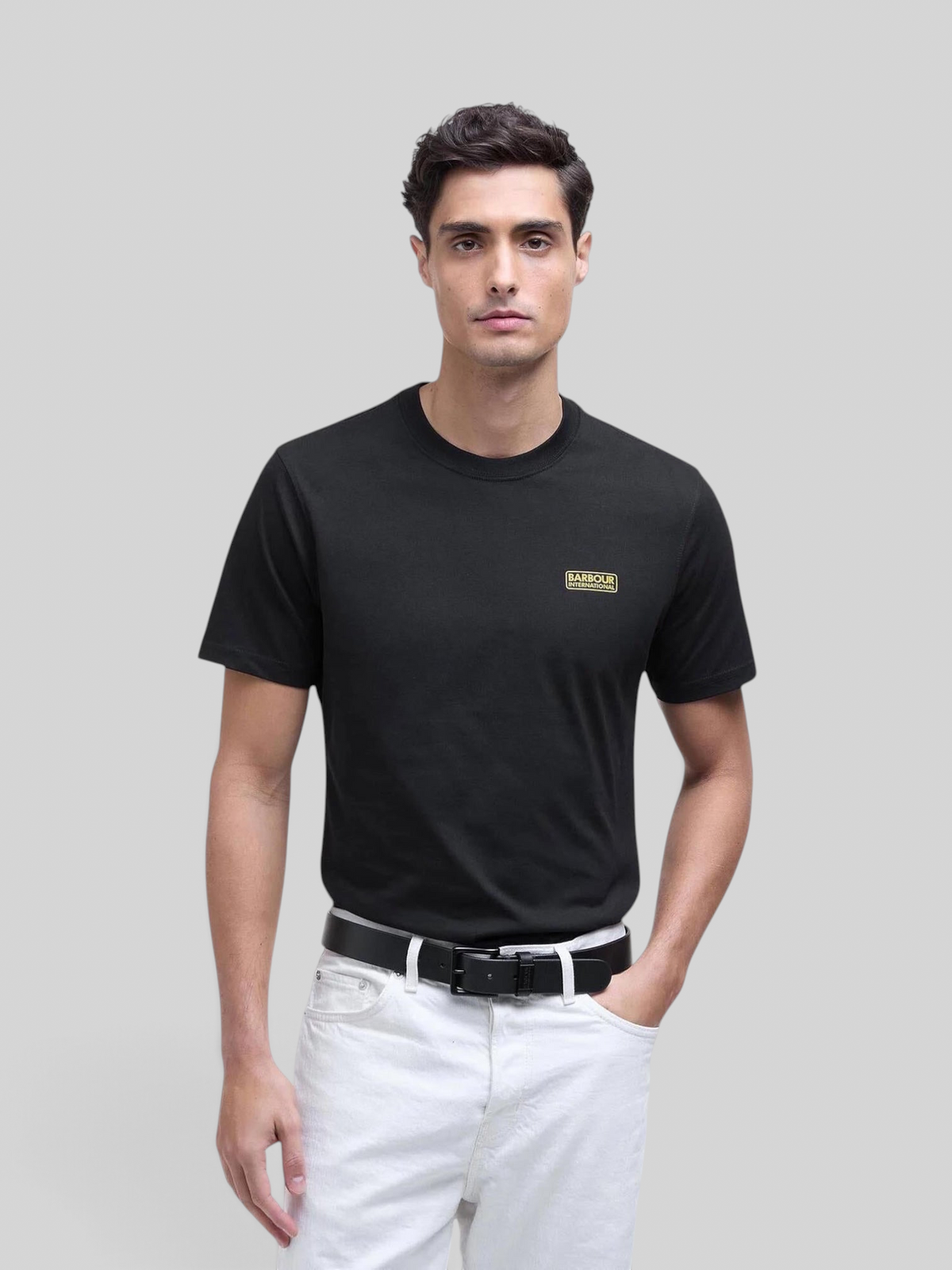 Baffle Haus black cotton crew neck t-shirt with small yellow chest logo worn by a male model with white jeans