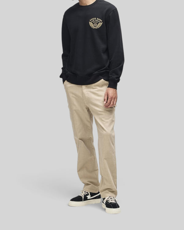 Baffle Haus Munificence black crew neck fleece with chest graphic, worn with beige trousers and black sneakers.