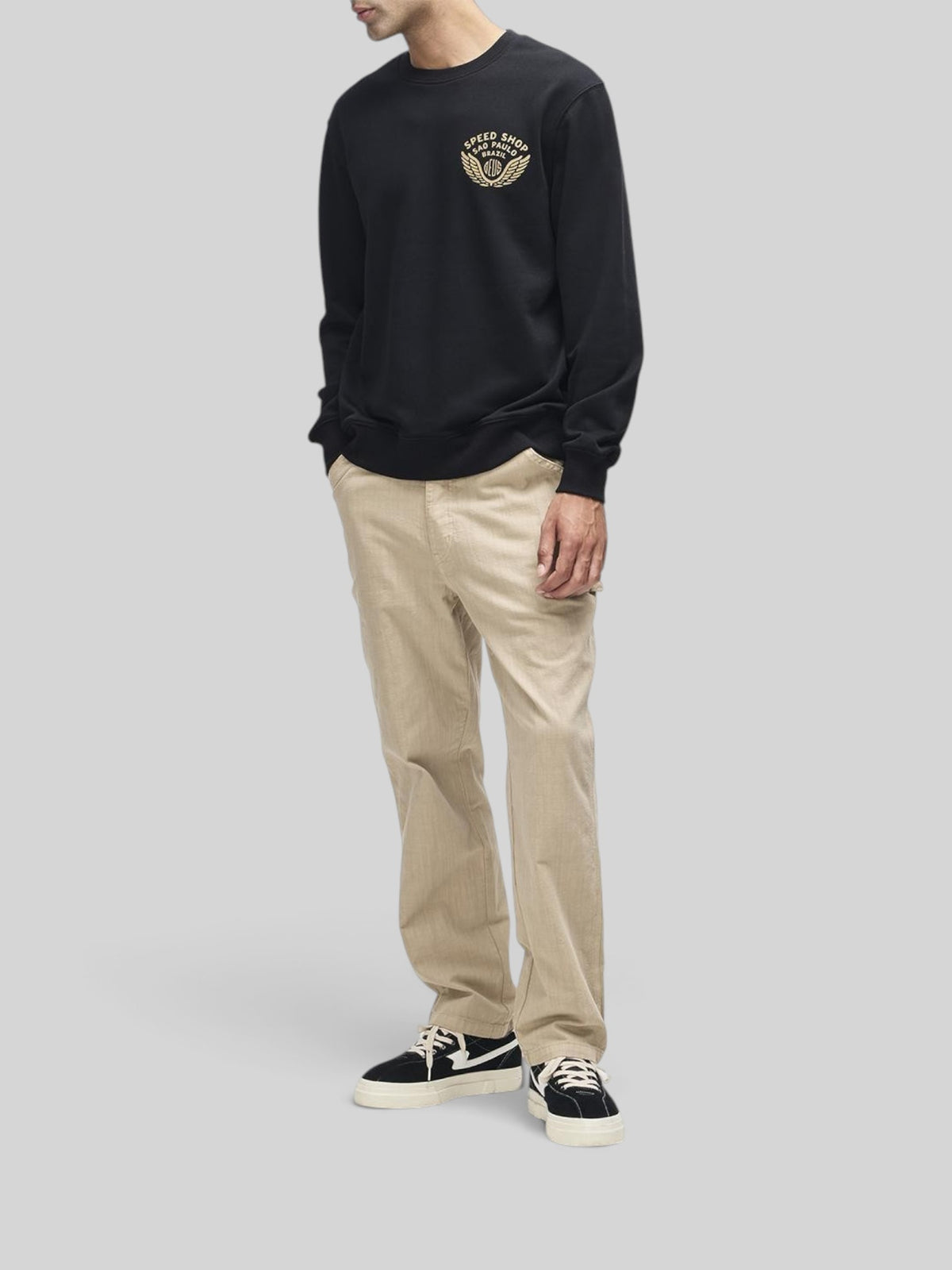 Baffle Haus Munificence black crew neck fleece with chest graphic, worn with beige trousers and black sneakers.