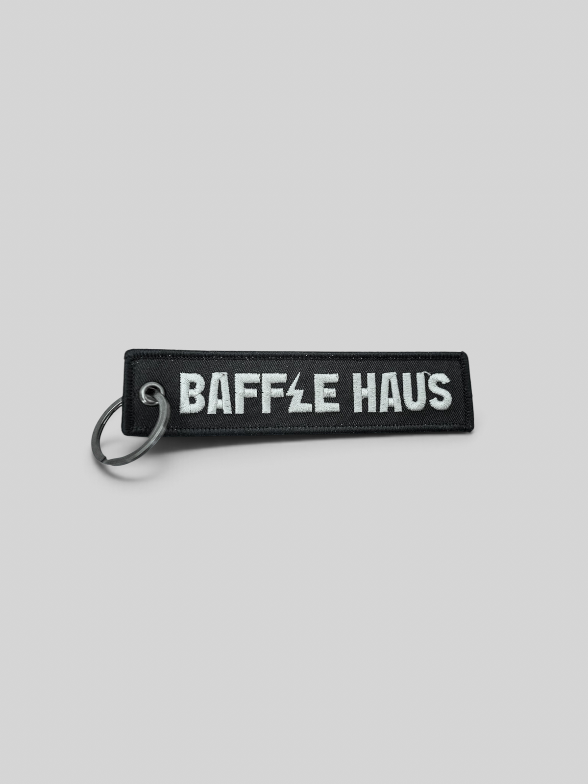 Baffle Haus black embroidered fabric keyring with white logo text and a durable metal ring attachment.