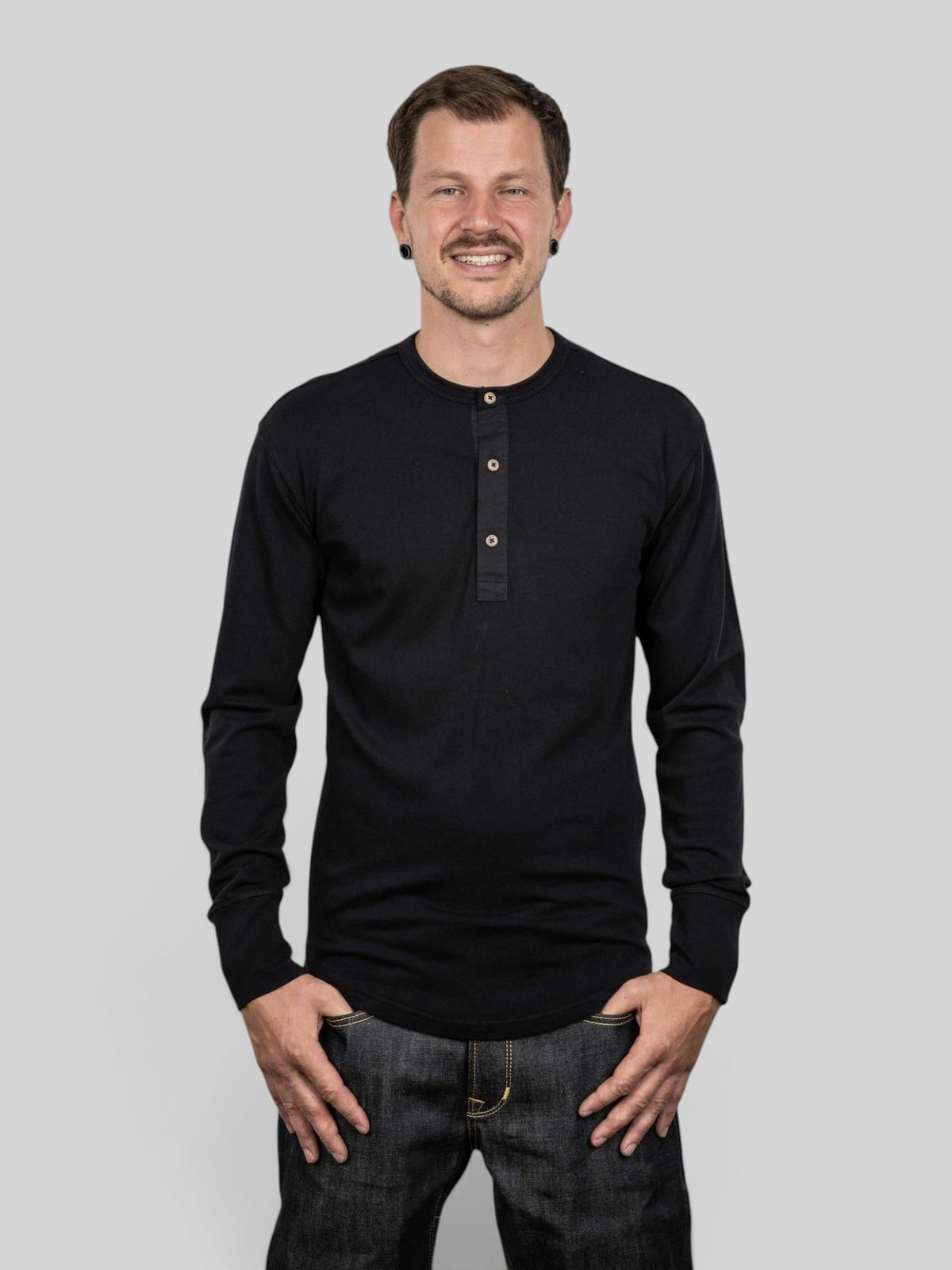 Baffle Haus 1927 long sleeve henley shirt in deep black cotton with coconut buttons worn by a smiling man