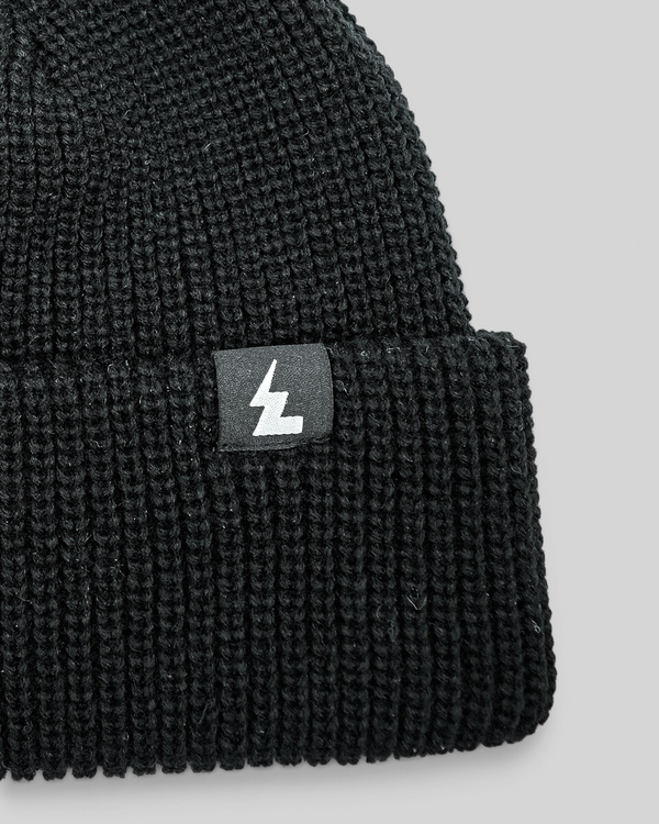 Baffle Haus black acrylic knit beanie with a classic ribbed texture and a small woven logo patch on the cuff.