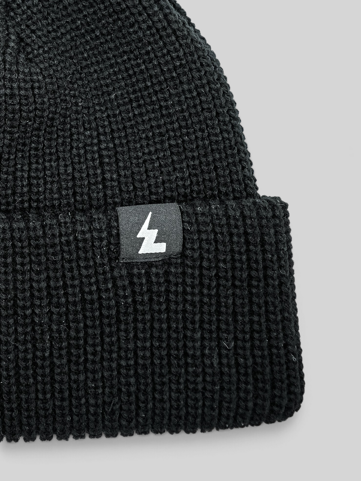 Baffle Haus black acrylic knit beanie with a classic ribbed texture and a small woven logo patch on the cuff.