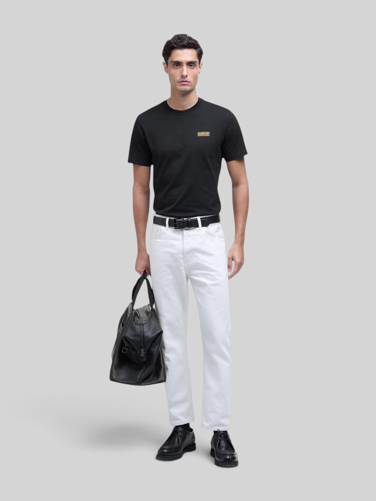 Baffle Haus black cotton crew neck t-shirt with small yellow chest logo worn by a male model with white jeans