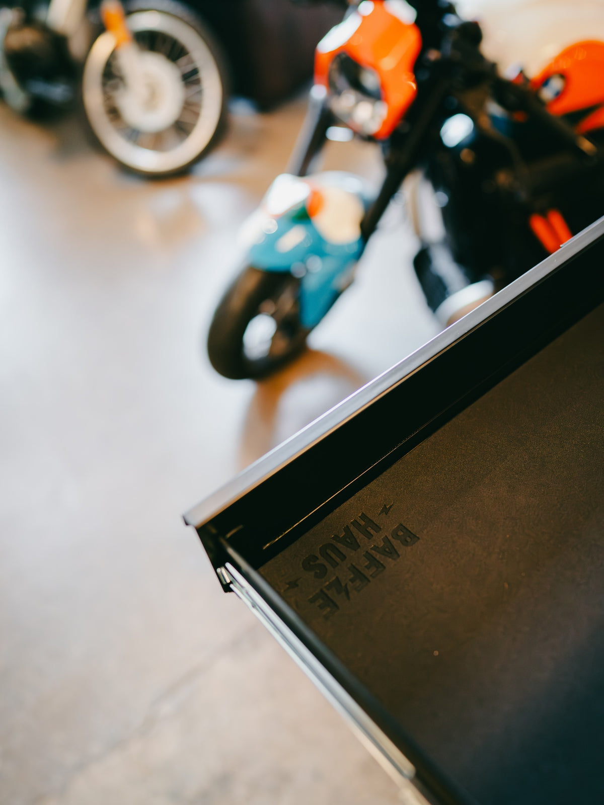 Open drawer of a black metal Baffle Haus tool box with branded logo detail in a motorcycle workshop setting