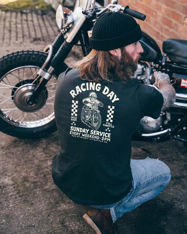 Baffle Haus black cotton t-shirt with vintage motocross screen print on back, worn by man working on a motorcycle.