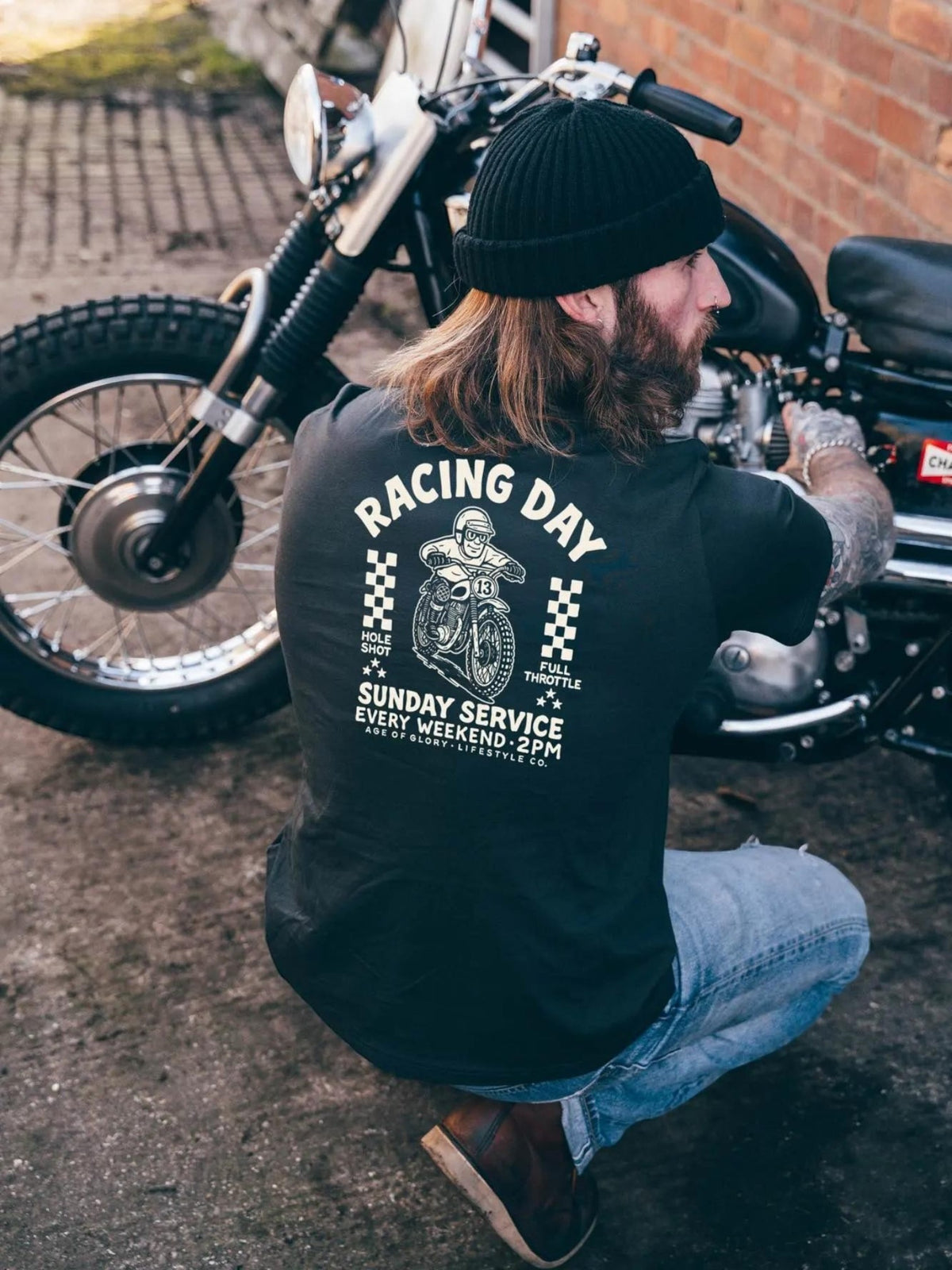 Baffle Haus black cotton t-shirt with vintage motocross screen print on back, worn by man working on a motorcycle.