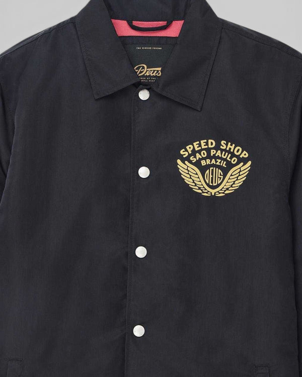 Baffle Haus Munificence black recycled nylon coach jacket with gold Speed Shop Brazil chest print and snap buttons.
