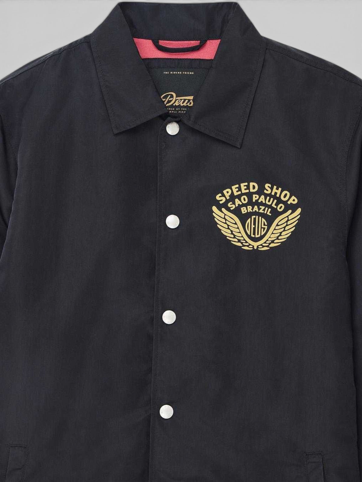 Baffle Haus Munificence black recycled nylon coach jacket with gold Speed Shop Brazil chest print and snap buttons.