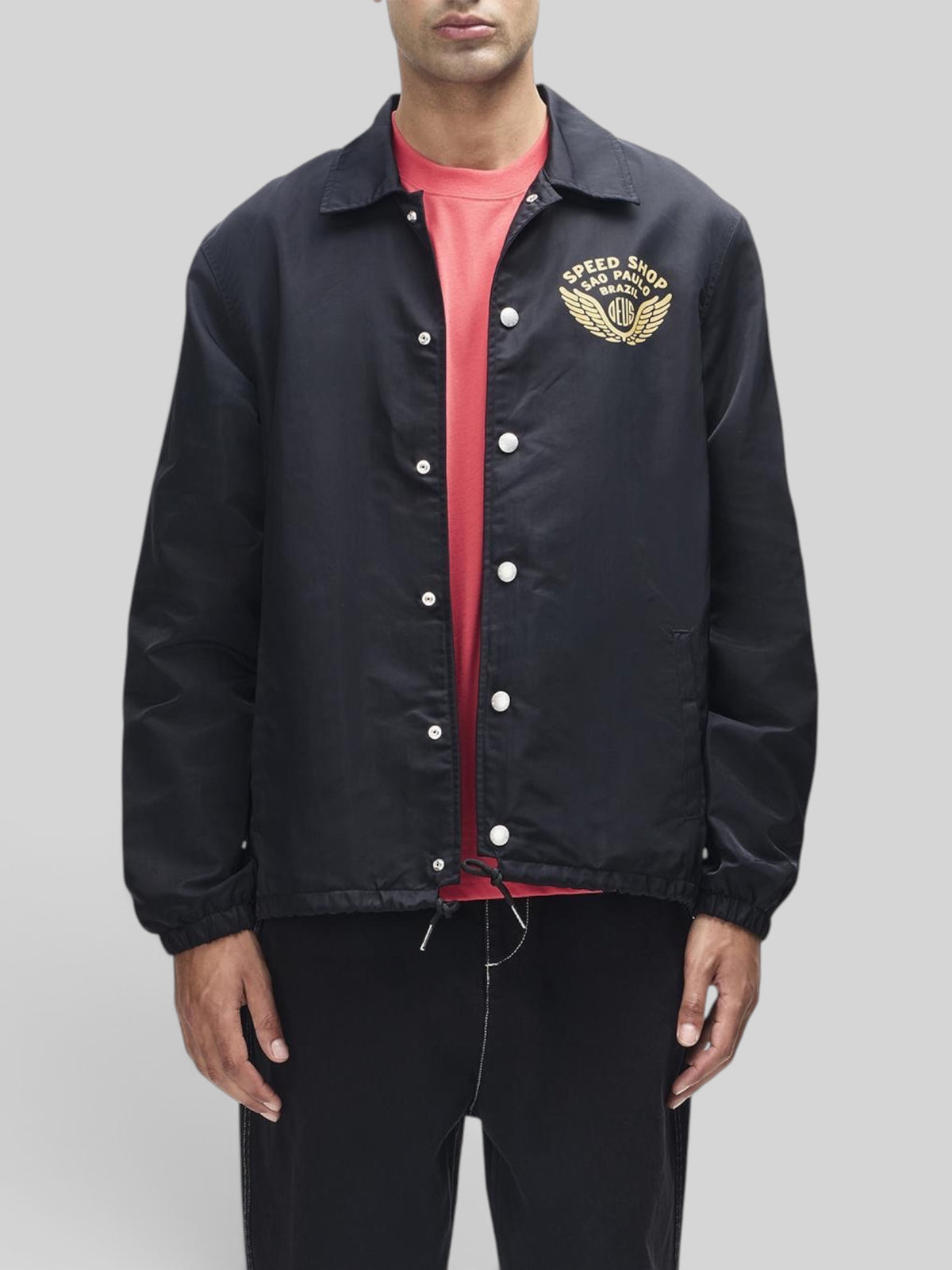 Baffle Haus Munificence black recycled nylon coach jacket with gold chest graphic and snap button closure