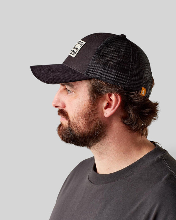 Side profile of a man wearing a black Baffle Haus trucker cap with a structured front and breathable mesh back.